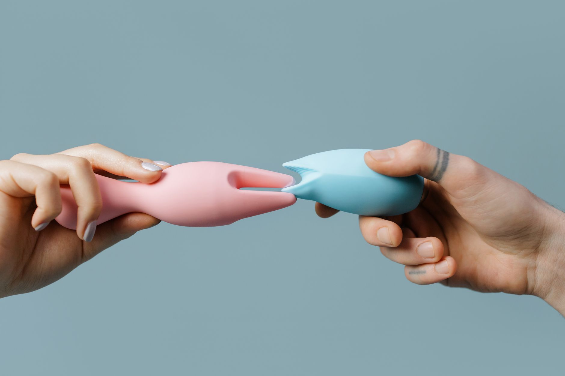 Hands holding pastel-colored silicone toys against a neutral background.