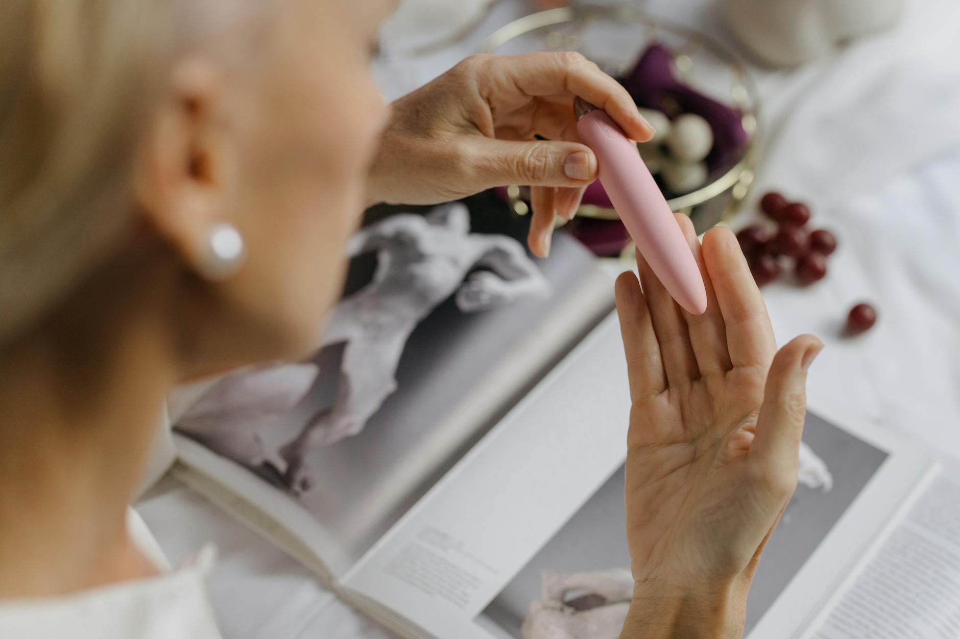 Close-up of hands exploring a lemon clitoral vibrator with books nearby, emphasizing intimate personal discovery