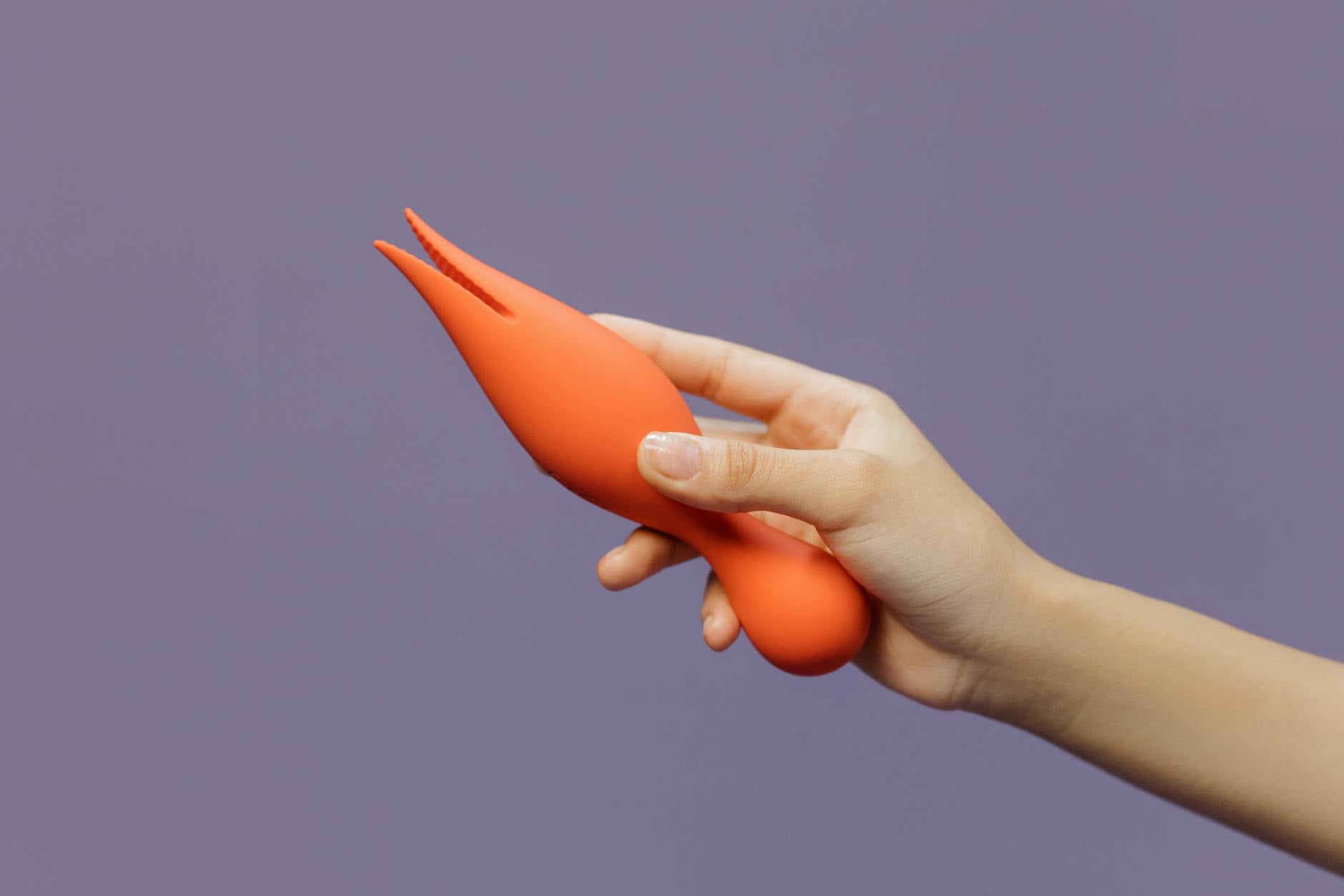 A hand holding a modern lemon vibrator against a minimalistic purple backdrop