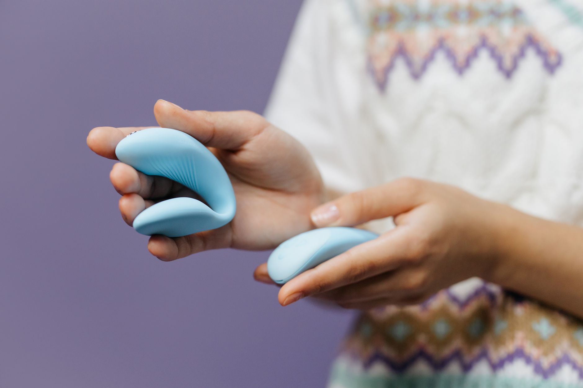 A hand holding a sleek blue vibrator against a purple background, showcasing modern pleasure tools