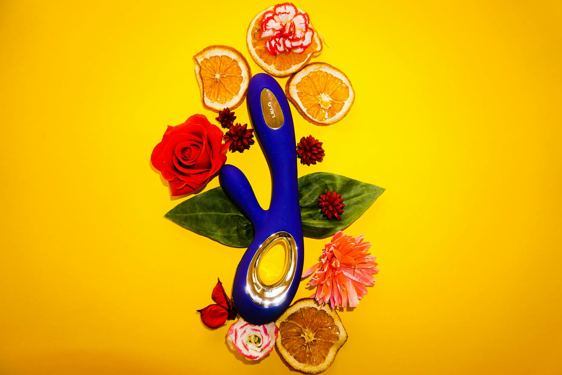 Blue Lemon vibrator surrounded by flowers and citrus on a bright yellow background.